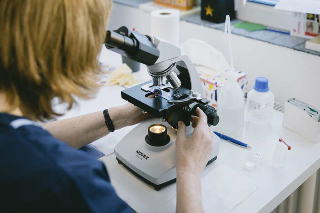 Mitarbeiterin untersucht eine Probe unter dem Mikroskop im hauseigenen Praxislabor.
